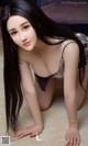 A woman with long black hair is posing on the floor.