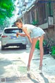 A woman in a white top and denim shorts leaning over a car.