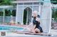 A woman sitting on the ground next to a swimming pool.