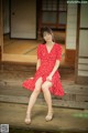 A woman in a red dress sitting on a wooden bench.