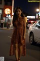 A woman in a brown dress standing in the middle of a street.