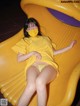 A woman in a yellow dress is sitting on a yellow slide.