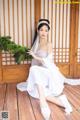 A woman in a white dress sitting on a wooden floor.