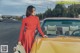 A woman in a red dress standing next to a yellow car.