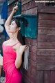 A woman in a pink dress leaning against a wooden wall.