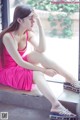 A woman in a pink dress sitting on a window sill.