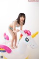 A young girl in a bikini standing on an inflatable unicorn.