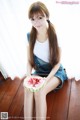 A woman sitting on a wooden floor holding a slice of watermelon.