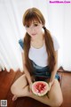 A woman sitting on the floor holding a slice of watermelon.