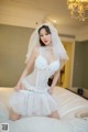 A woman in a wedding dress sitting on a bed.