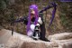 A woman with purple hair sitting on a rock holding a bow and arrow.