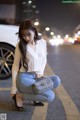 A woman sitting on the side of a road next to a car.