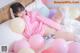 A woman laying on a bed with pink and white balloons.