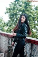 A woman in a black leather jacket leaning against a wall.