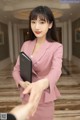 A woman in a pink suit holding a black folder.