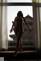 A naked woman standing in front of a window.