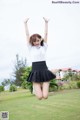 A woman in a white shirt and black skirt jumping in the air.