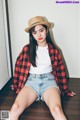 A woman sitting on the floor wearing a hat and a plaid shirt.