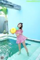 A woman in a pink dress holding a yellow ball in a pool.