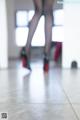 A woman in black stockings and high heels standing on a tiled floor.